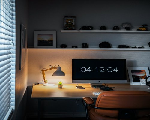 A home office setup on a rainy, grey afternoon with a warm desk lamp turned on